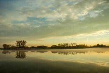 Fototapeta na wymiar Fog over a calm lake, trees and evening clouds