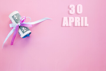 calendar date on pink background with rolled up dollar bills pinned by pink and blue ribbon with copy space. April 30 is the thirtieth day of the month