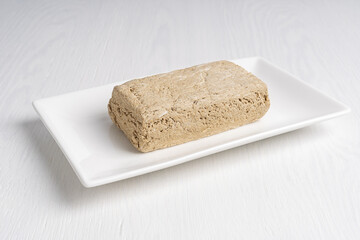 Halva, also halvah, asian turkish homemade local sweet dessert made of fried sunflower seeds grinded to paste and sugar syrup served on rectangular plate on white wooden background. Horizontal image