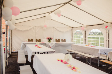 Tables and benches in a wedding tent decorated with white and pink balloons