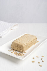 Halva, also halvah or halwa, asian turkish homemade sweet dessert made of fried sunflower seeds and sugar syrup served on rectangular plate on white wooden background with textile towel. Vertical