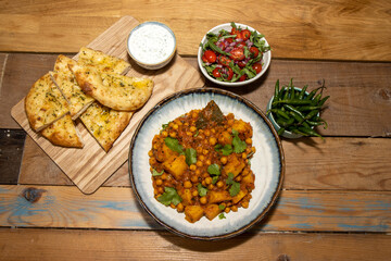 A bowl of the delicious Indian dish Chana Masala made from chickpeas and potatoes on a wooden kitchen table