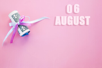 calendar date on pink background with rolled up dollar bills pinned by pink and blue ribbon with copy space.  August 6 is the sixth day of the month