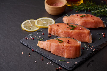 Fresh fish. piece of raw salmon fish fillet, spices on a black stone surface, Delicious fish meat. top view. Healthy food.
