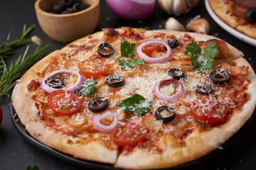 Italian pizza and pizza cooking ingredients on black concrete background. Tomatoes on vine, mozzarella, black olives, herbs and spices. Mixture pizza Italian food. Copy Space. Top view.