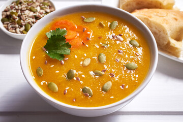 Pumpkin soup-puree with curry seasoning, whole grains and sesame seeds. Vegan Indian food on a white wooden table.