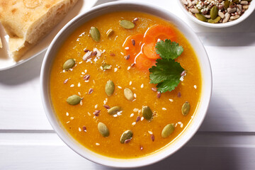 Pumpkin soup-puree with curry seasoning, whole grains and sesame seeds. Vegan Indian food on a white wooden table.