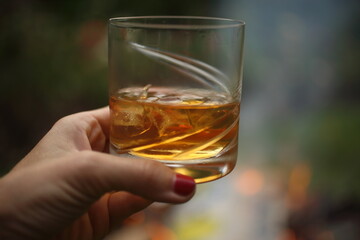 Hand holding full whiskey glass at fireplace
