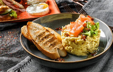 Delicious breakfast with scrambled eggs with salmon on top, salad, and toast on plate over dark background. Healthy breakfast concept, close up