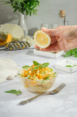 Woman squeezes lemon into a salad of cabbage, grated carrot with basil and rosemary