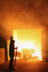 Fireman stands in front of a burning house full of flames and tries to extinguish the house. silhouette of a firefighter