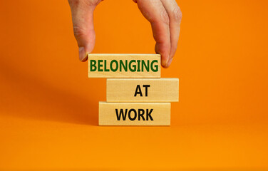 Belonging at work symbol. Wooden blocks with words 'Belonging at work' on beautiful orange background. Businessman hand. Business, belonging at work concept. Copy space.