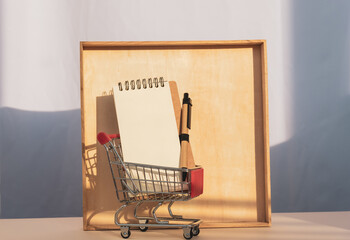 Mini trolley cart with white card casting a shadow on wooden frame. Copy space, template.