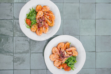 Mediterranean meal with shrimps, octopuses, seaweed and caviar in plates on green tiles, view from above