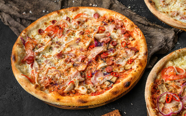 Pizza Pepperoni with prosciutto, sausage, cheese parmesan, tomatoes and onion rings on stone black background. Fast food lunch for picnic company, top view, selective focus