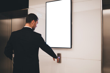 Businessman calling lift in modern hallway with blank info billboard © BullRun