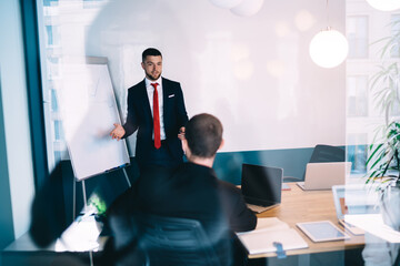 Coworkers discussing business project in conference hall with various gadgets and flip chart