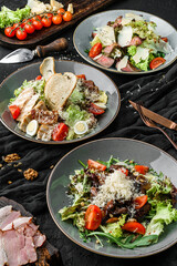 Assorted healthy salads with meat, green leaves, tomatoes, and parmesan. Chicken salad on dark background. Healthy vegan food, clean eating, dieting, top view
