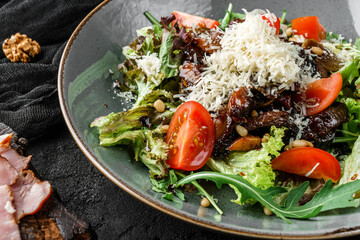Tasty steak salad in balsamic sauce with tomatoes, green leaves, and parmesan on dark background. Healthy vegan food, clean eating, dieting, top view