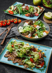 Assorted healthy salads with salmon, steak, avocado, tomatoes, and green leaves on dark background, close up view. Healthy food, clean eating, dieting