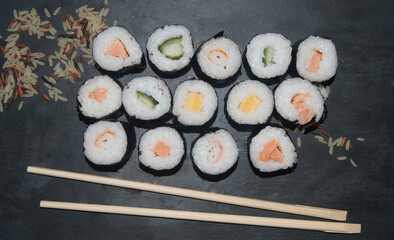Variety of sushi with soy sauce in a bowl and chopsticks served on black table