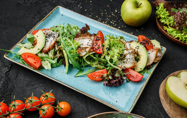 Summer salad with grilled salmon, green leaves, arugula, avocado, and tomato on dark background, close up view. Healthy food, clean eating, dieting