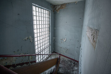 Staircase of an abandoned interior with windows made of glass blocks and walls painted blue in the...