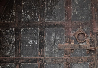 Grunge background from a black old metal door with a bolt and a ring. The door to the old castle.