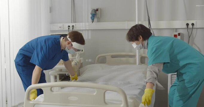Medical staff changing linen of bed in empty hospital ward