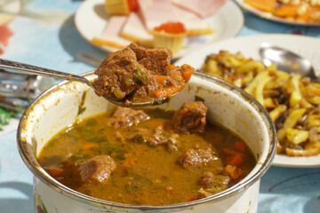 A piece of meat on a spoon over a saucepan with cooked stew.