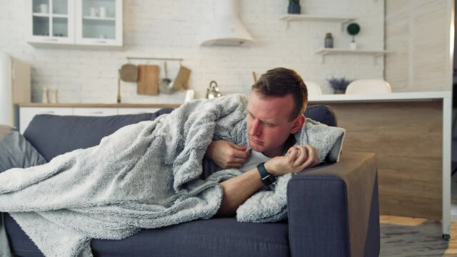 Man feeling sick on the couch at home with cold and flu symptoms. Pandemic.
