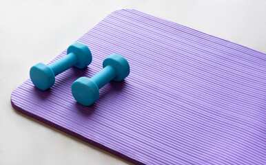 Close up of a light blue dumbbell on a violet yoga pilates mat on the floor of a gym