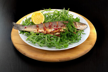 Whole Sea Bass on a bed of rocket, arugula, with lemon,pink peppercorns and a sprig of dill, part of a healthy,delicious mediterranean diet