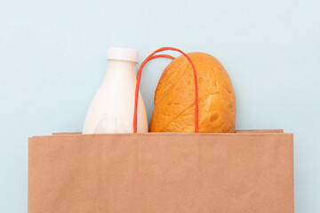 Paper bag with bottle of milk and loaf, white bread on blue background