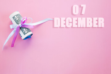 calendar date on pink background with rolled up dollar bills pinned by pink and blue ribbon with copy space.  December 7 is the seventh day of the month