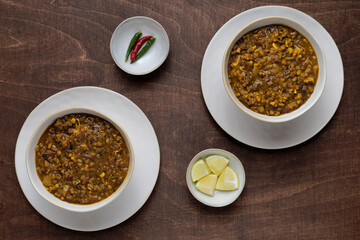 Two whole mung bean curry plates with limes and chili on wooden table. Flat lay, top view.