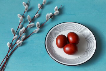 Naklejka na ściany i meble Ester brown eggs (colored with onion peel) on a plate and pussy willow branch on blue wooden table background.