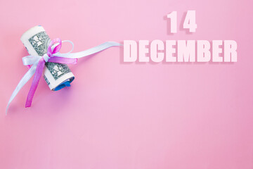 calendar date on pink background with rolled up dollar bills pinned by pink and blue ribbon with copy space. December 14 is the fourteenth  day of the month