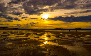 Obraz premium El sol y las abundantes nubes se reflejan en los charcos de la bajamar en la playa de Somo, España