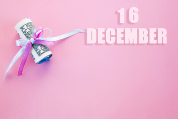 calendar date on pink background with rolled up dollar bills pinned by pink and blue ribbon with copy space. December 16 is the sixteenth day of the month