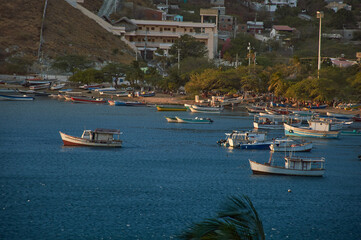 Fototapeta na wymiar Playa de santa marta con diferentes barcos de pescaderos y lanchas a las 6 pm de la tarde con casa y edificios entre los arboles y la montaña