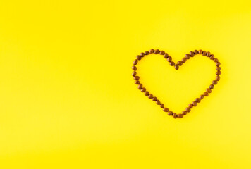 Heart from coffee beans on yellow background with copy space. Minimal love concept on illuminating background.