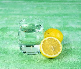 A glass with water and a slice of lemon on a green light background.