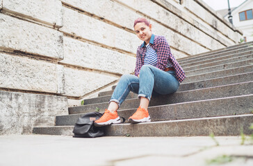 Portrait of smiling Beautiful modern young female teenager with extraordinary hairstyle color in checkered sitting on the old town stairs. Modern teens or young students concept image.