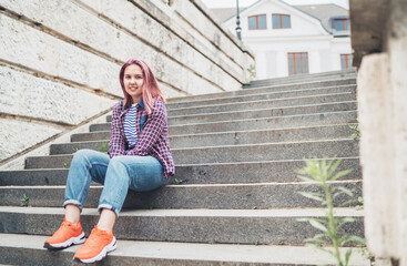 Portrait of smiling Beautiful modern young female teenager with extraordinary hairstyle color in checkered sitting on the old town stairs. Modern teens or young students concept image.