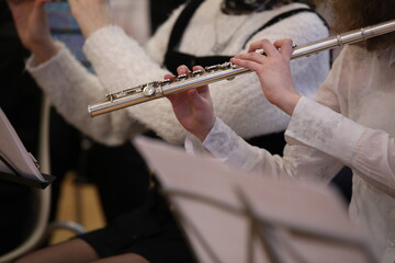 A student girl plays a musical instrument in her hands a silver flute fingers on the flaps in a uniform white blouse black skirt at a class in the school orchestra.Details.Selective Focus © Nina