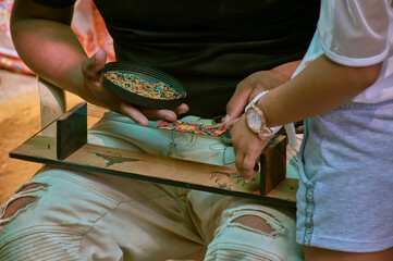 Jóvenes trabajando en manilla de bolitas artesanal en tabla de madera con muchos cuidado de diferentes colores cálido © Esteban.94c