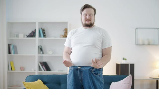 Happy young man showing oversize trousers, weight loss plan, transformation