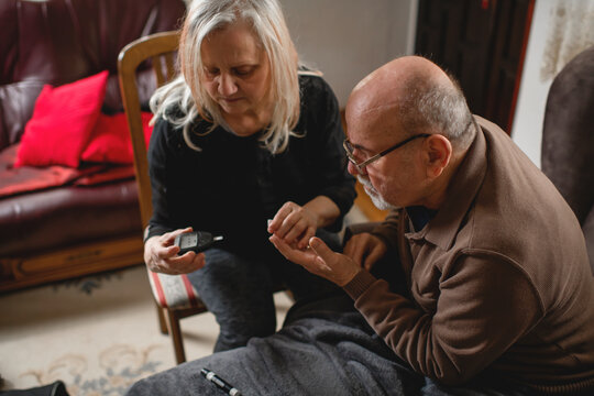 Senior woman checking blood sugar of her diabetic husband at home
