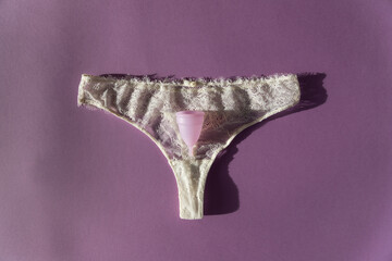 Sexy lingerie lace thong for women with a pink menstrual cup on top. Being sexy when on the period concept.